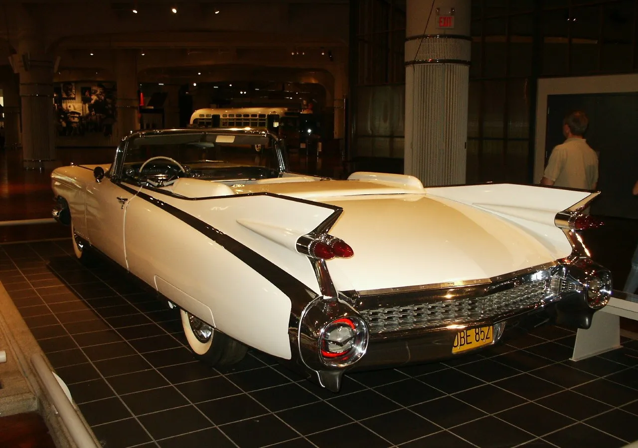 The rear of a white 1959 Cadillac convertible on a museum floor, with tall pointed tailfins and twin bullet taillights on each side